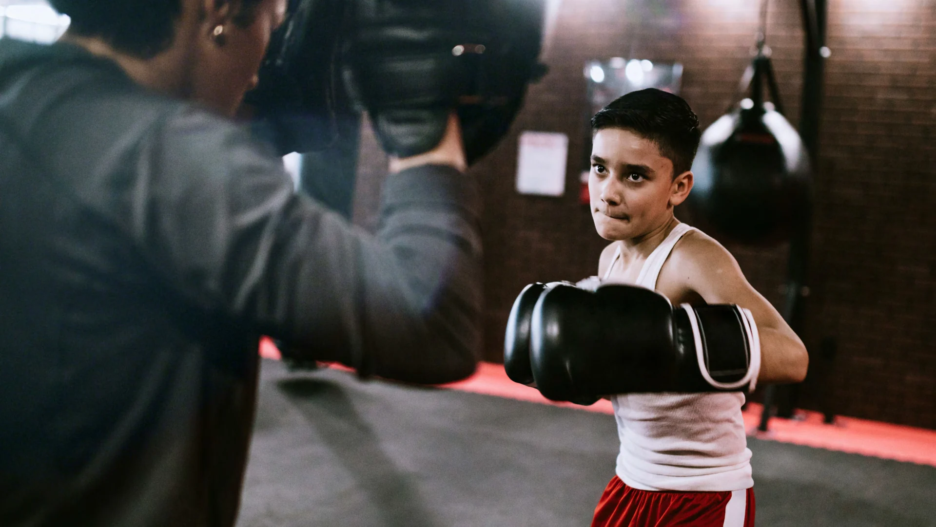A young boxer practising with a coach holding pads
